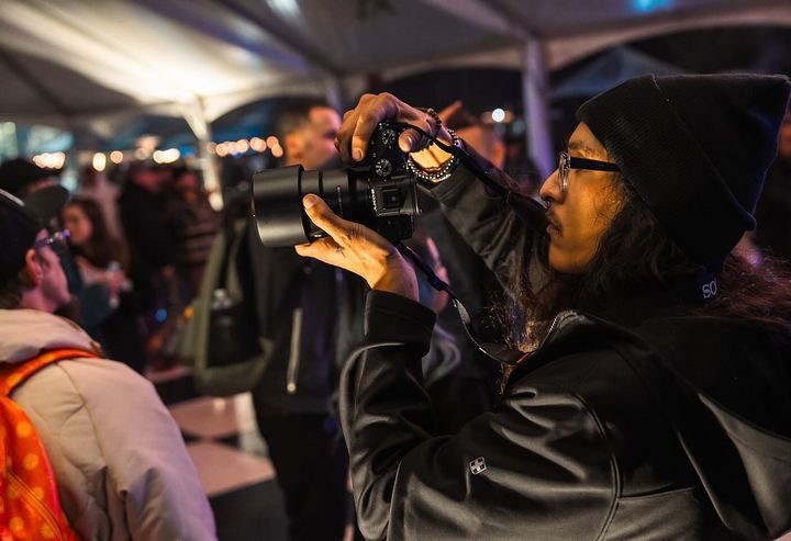 Gabe shooting at an event, camera raised, shot by someone else